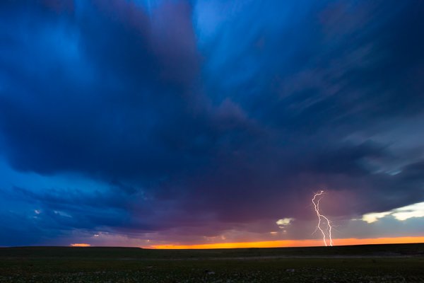 A CG (cloud to ground) lightning bolt strikes in a field somewhere in east Texas as a storm moves off in the distance.